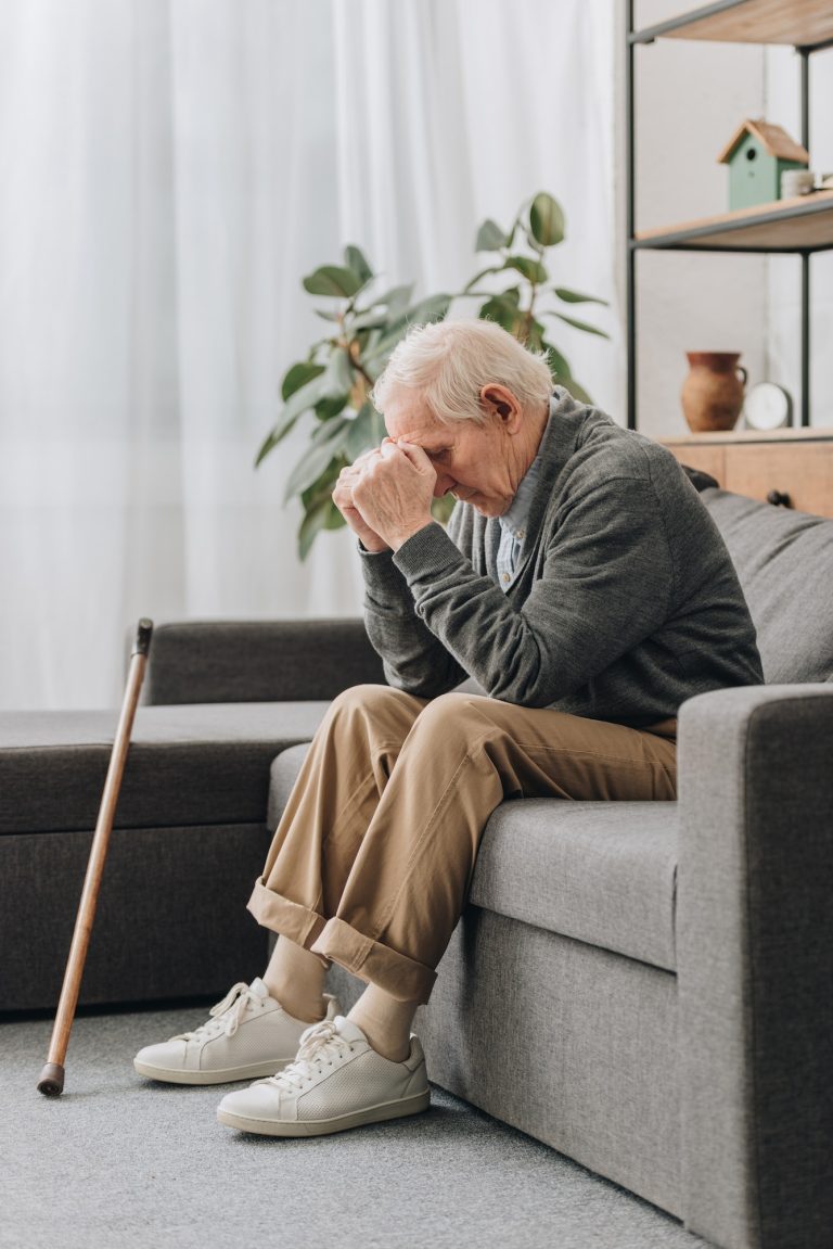 upset male pensioner sitting on sofa near walking cane